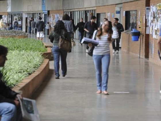 Estudantes circulam pelo corredor de uma universidade pública brasileira, carregando mochilas e materiais de estudo.