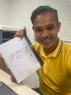 Homem de camisa amarela com sua tese de doutorado