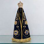 Imagem de Nossa Senhora Aparecida com manto azul-marinho bordado em dourado e coroa ornamentada.