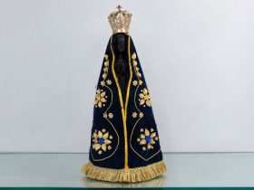 Imagem de Nossa Senhora Aparecida com manto azul-marinho bordado em dourado e coroa ornamentada.