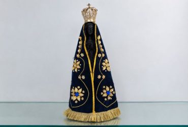 Imagem de Nossa Senhora Aparecida com manto azul-marinho bordado em dourado e coroa ornamentada.