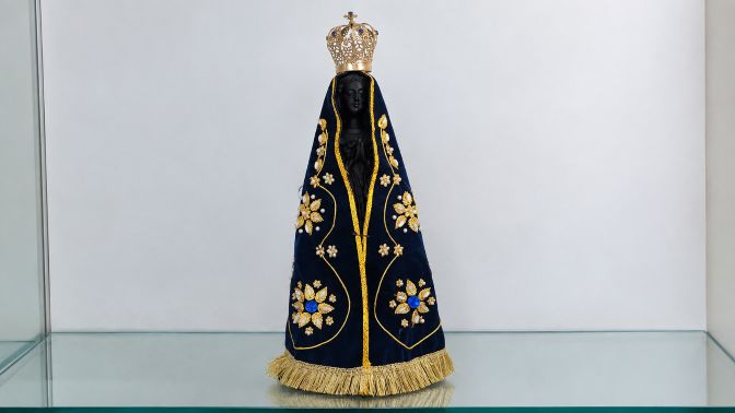 Imagem de Nossa Senhora Aparecida com manto azul-marinho bordado em dourado e coroa ornamentada.