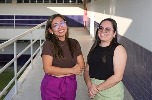 Duas pesquisadoras da UFC posam lado a lado em corredor de universidade.