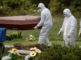 Profissionais vestidos com equipamentos de proteção individual transportam um caixão em um cemitério durante a pandemia de Covid-19.