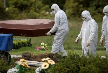 Profissionais vestidos com equipamentos de proteção individual transportam um caixão em um cemitério durante a pandemia de Covid-19.
