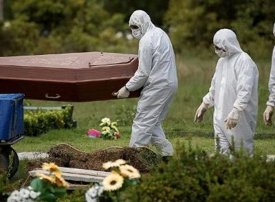 Profissionais vestidos com equipamentos de proteção individual transportam um caixão em um cemitério durante a pandemia de Covid-19.