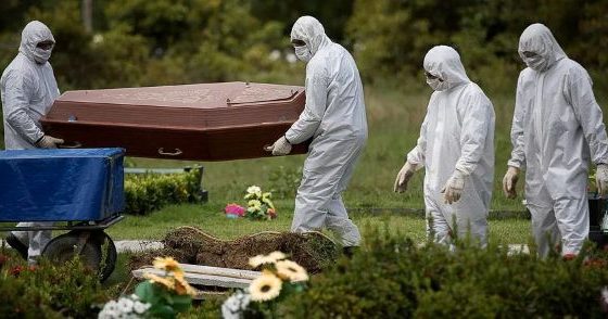 Profissionais vestidos com equipamentos de proteção individual transportam um caixão em um cemitério durante a pandemia de Covid-19.