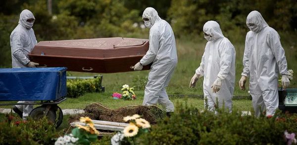 Profissionais vestidos com equipamentos de proteção individual transportam um caixão em um cemitério durante a pandemia de Covid-19.