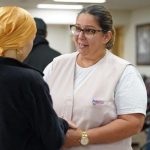 Profissional de saúde conversa com paciente usando lenço na cabeça em sala de espera.