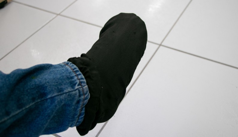 Pé coberto por meia preta, com parte da perna coberta por calça jeans.